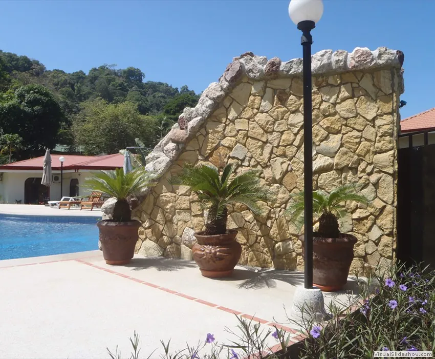 Muro de piedra mollejón junto a una piscina en un entorno tropical con palmas — Deco Rock, Costa Rica