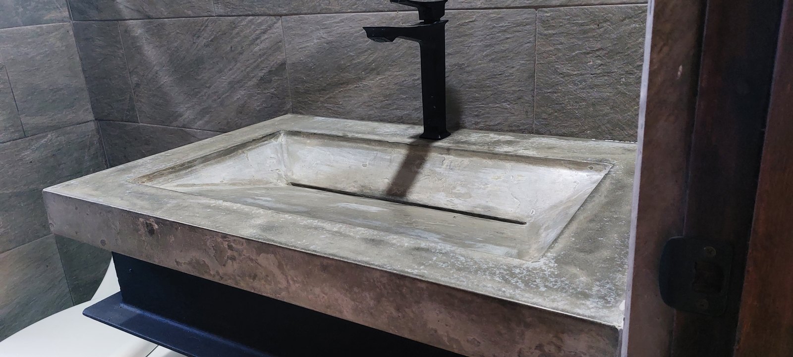 Lavamanos de concreto gris con grifo negro sobre mueble oscuro